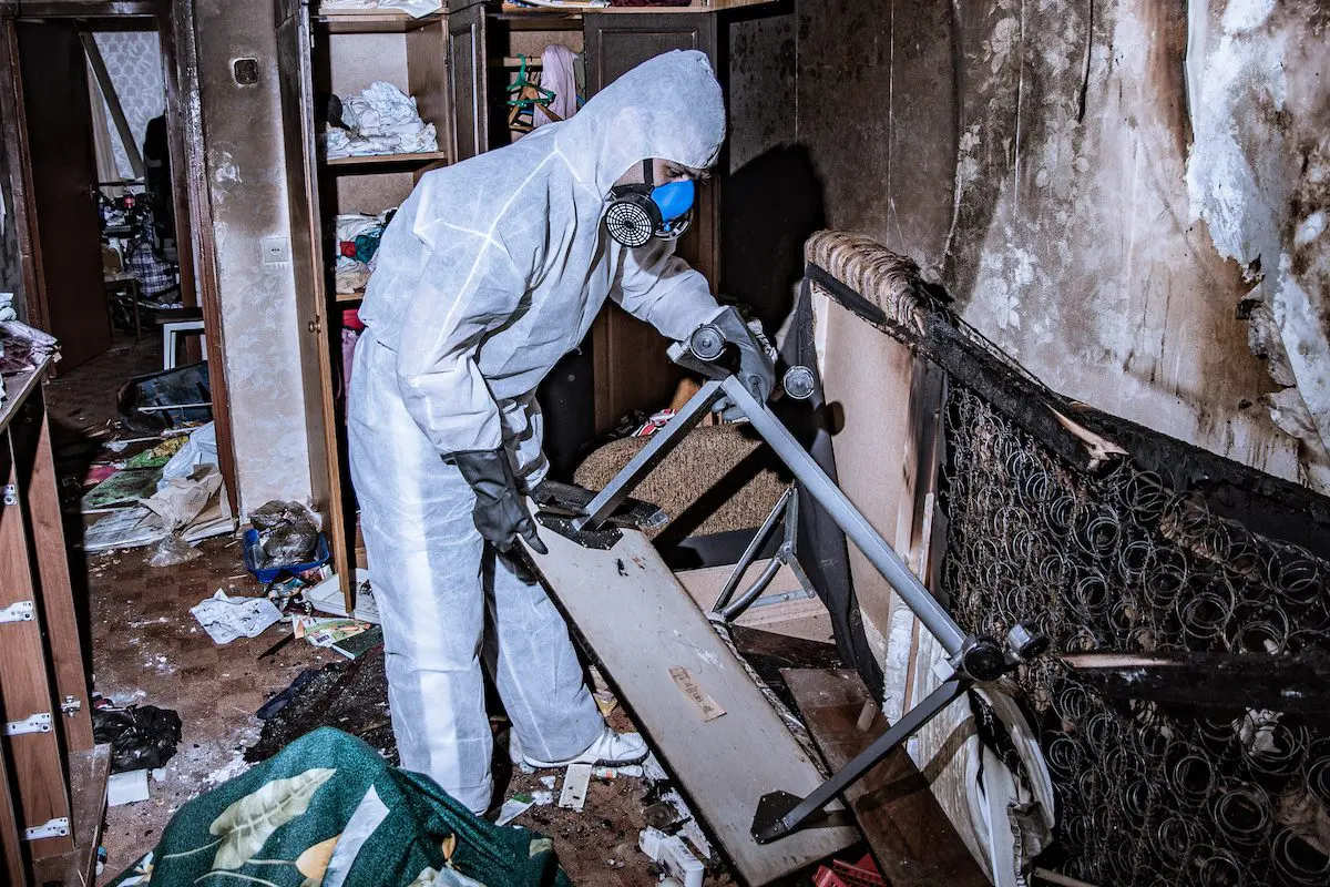 Dos and Don'ts After a House Fire: Your Guide to Fire Damage Restoration - Flood Response A fire damage restoration specialist in a protective suit from a cleaning company cleans a destroyed housing after a fire.