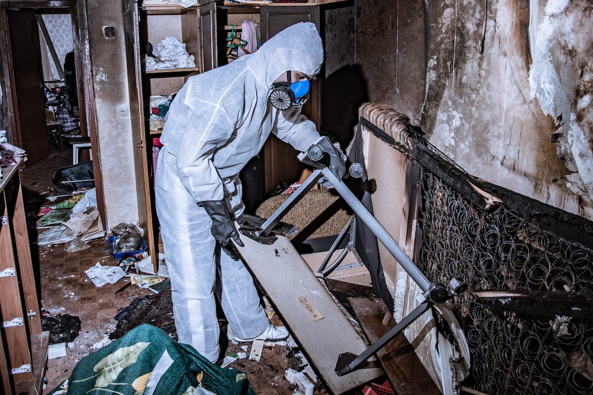 A fire damage restoration specialist in a protective suit from a cleaning company cleans a destroyed housing after a fire.