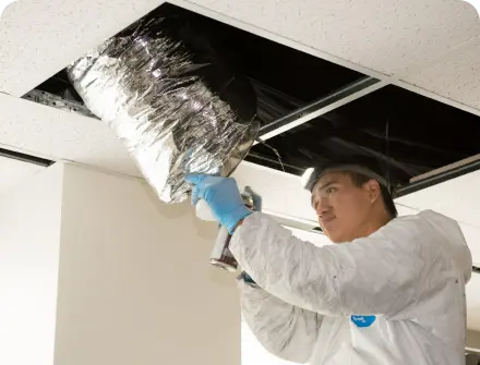 A worker inspecting an air duct in a commercial building